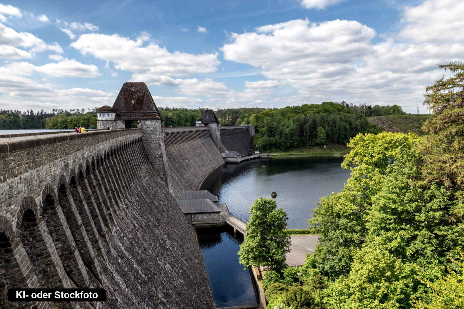 Die Staumauer der Möhnetalsperre mit ihren beiden Türmen, dahinter der Möhnesee und bewaldete Ufer